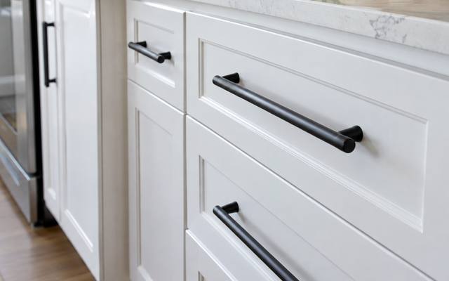Black bar pulls mounted on freshly painted white cabinet doors.