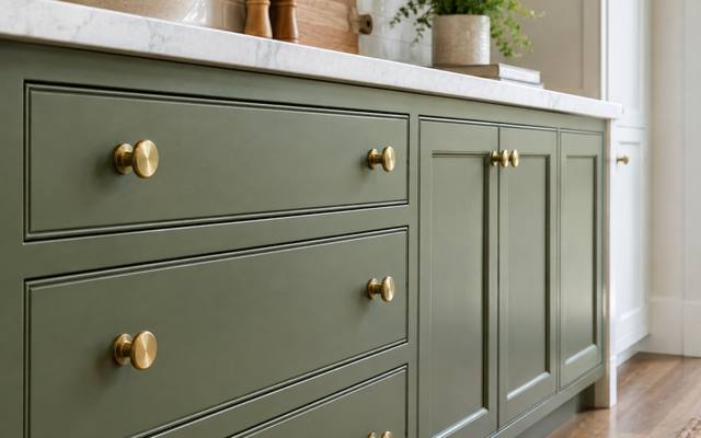 A close view of sage green drawer fronts fitted with brass knobs.